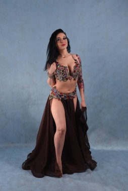 Oryantal elbiseli güzel bir dansçı stüdyoda mavi arka planda dans ediyor kahverengi etek ve elbisesini sallıyor.