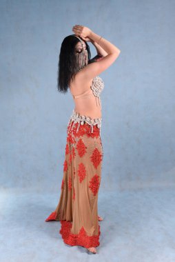 Çiçekli etekli güzel bir dansçı arkasında mavi bir arka planla stüdyoda poz verir.