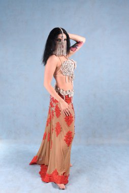 Çiçekli etekli güzel bir dansçı arkasında mavi bir arka planla stüdyoda poz verir.