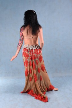 Çiçekli etekli güzel bir dansçı arkasında mavi bir arka planla stüdyoda poz verir.