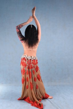 Çiçekli etekli güzel bir dansçı arkasında mavi bir arka planla stüdyoda poz verir.