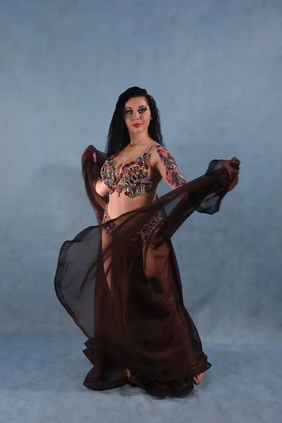 A beautiful dancer in an Oriental dress is dancing in the Studio on a blue background waving a brown skirt and dress