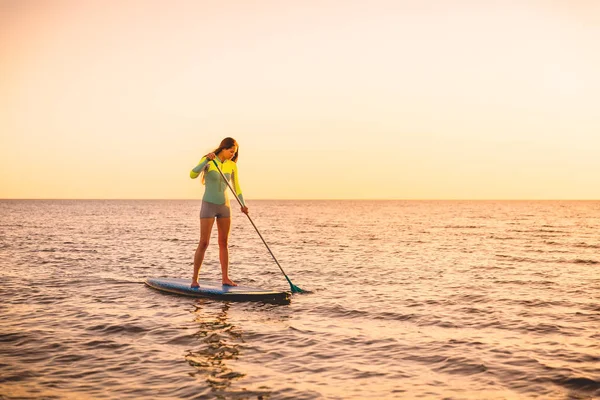 夕暮れ海でサーフボードに漕ぎサーフィンの魅力的な女性 — ストック写真