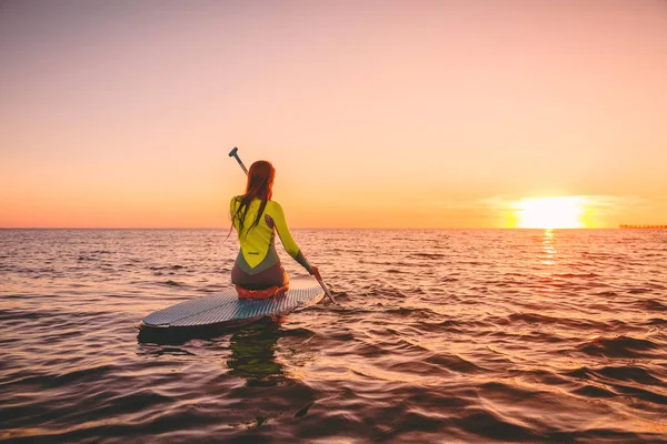 夕暮れ海でサーフボードに漕ぎサーフィン女性 — ストック写真