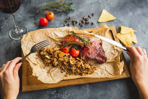烤猪肉排骨 荞麦与蘑菇和西红柿在老式木制切割板和妇女手用餐具 关闭视图 — 图库照片