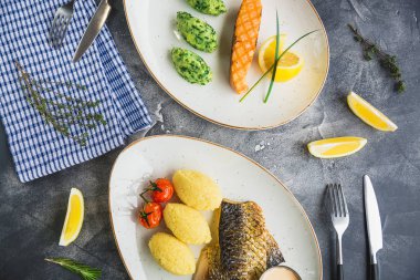 Balık yemekleri ve limon dilimleri gri arka plan üzerinde beyaz tabaklar. Görünümü kapatın