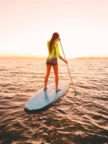 日没時に海でサーフボードに乗るスポーティな美人パドル — ストック写真