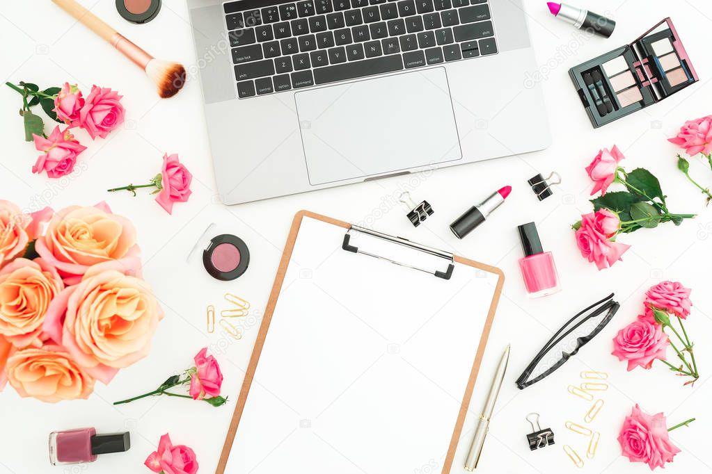 Laptop, clipboard, roses flowers, cosmetics and accessories on white background. Flat lay. Top view. Feminine freelancer office concept