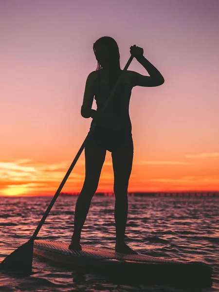 スタンド アップ パドル ボード暖かい夕焼け色に浮いている若い女性 — ストック写真