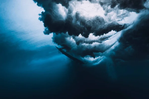 Surfer with surfboard dive underwater of big wave.