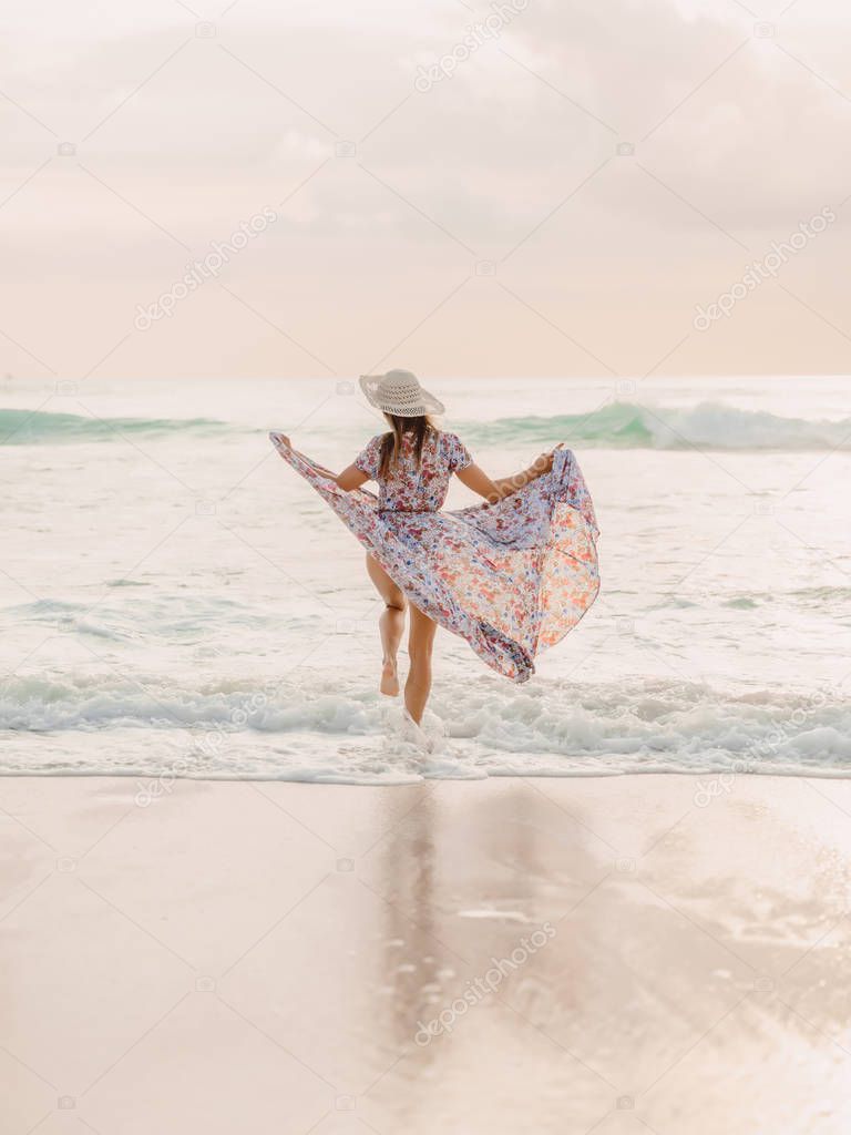 Attractive stylish woman in summer dress on beach at sunset or sunrise. Woman fashion.