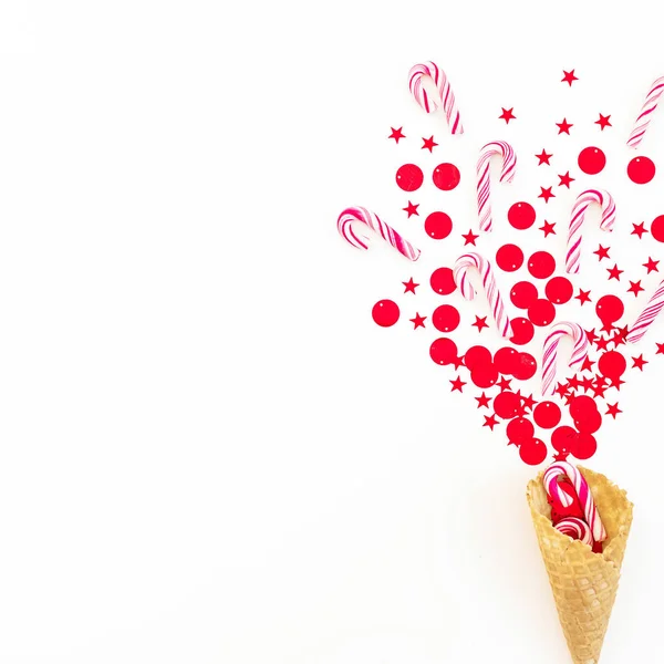 Christmas concept with red confetti, candy canes and waffle cone on white. Flat lay, top view. Copy space