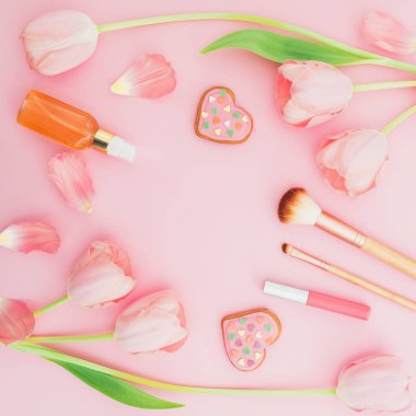 Çerçeve pembe çiçekler, kozmetik ve çerezleri pembe bir arka plan ile. Kopya alanı düz yatıyordu, en iyi manzaralı