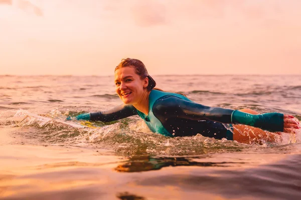 Attractive surfer woman on a surfboard swim in ocean. Surfing at sunset