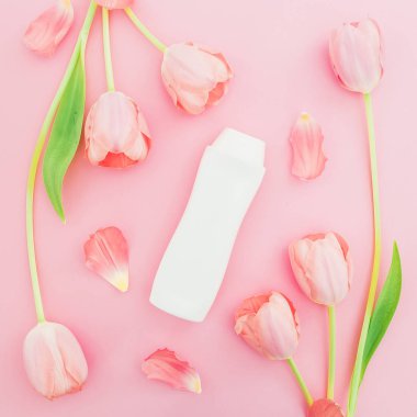 Şampuan şişesi ve pembe bir arka plan üzerinde beyaz lale çiçekler. Düz yatıyordu, en iyi görünümü