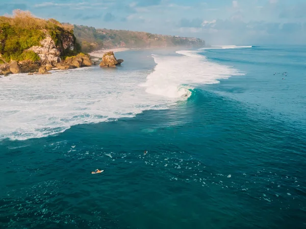 Aerial view of crashing wave in ocean with surfers and sunset light. Wave crashing on reef.