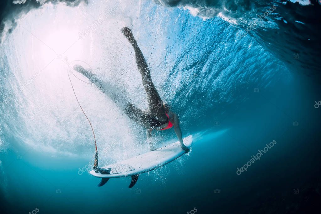 Surfer girl with surfboard dive with under ocean wave. Underwater view