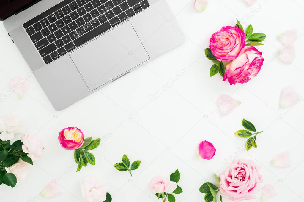 Frame with laptop, roses flowers and petals on white background. Flat lay. Top view. Feminine composition