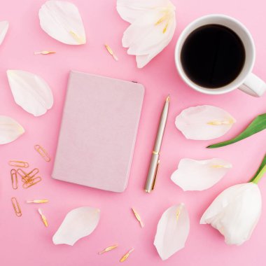 Beyaz Lale çiçek ve yaprakları bir fincan kahve, defter ve kalem üzerinde pembe bir arka plan ile. Blogger kavramı. Düz yatıyordu, en iyi görünümü.
