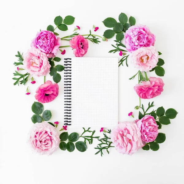 Floral frame of pastel pink roses, peonies and notebook on white background. Flat lay, top view. Spring time composition