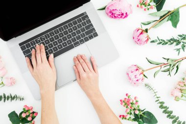 Dizüstü bilgisayarda yazarak kadın. Office çalışma alanıyla eller, laptop, dizüstü bilgisayar ve pembe çiçekler beyaz arka plan üzerinde. Üstten görünüm. Düz yatıyordu.