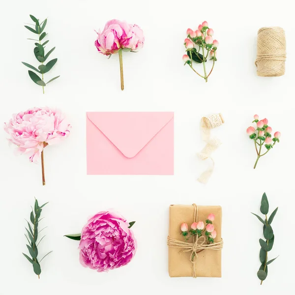 Floral composition with pink peonies, roses, hypericum and eucalyptus with envelope and gift box on white background. Flat lay, top view