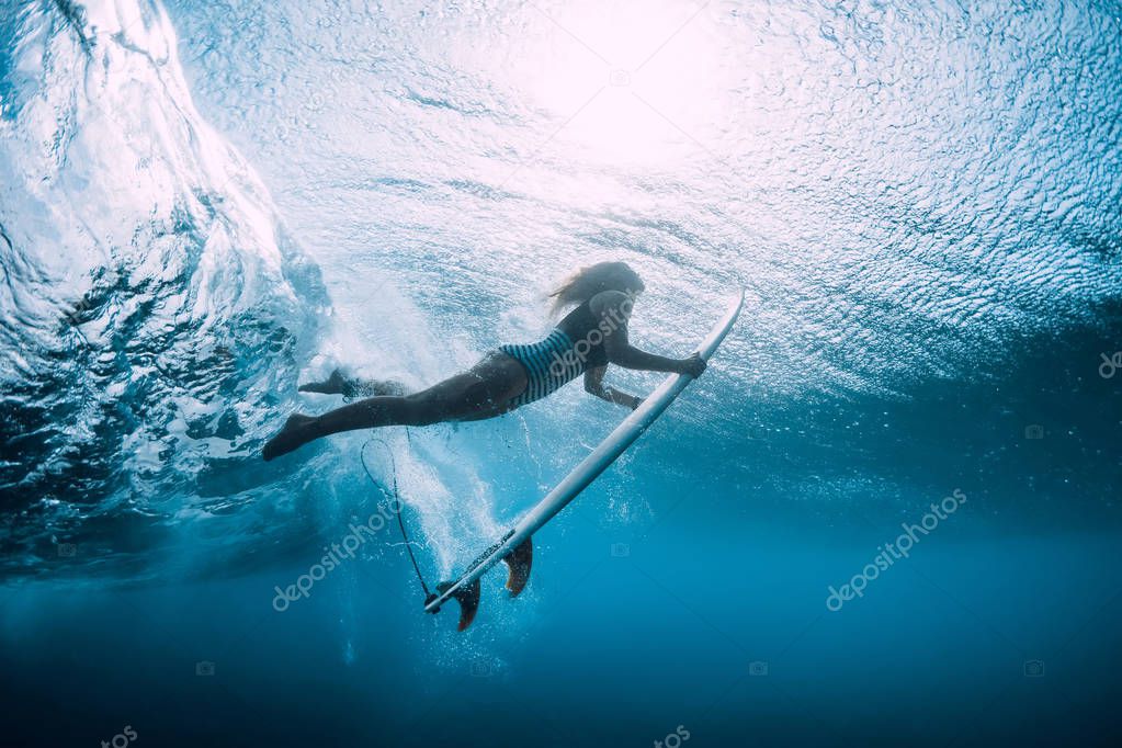 Surfer woman dive underwater with under wave.