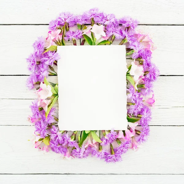 Pink flowers and card on white wooden background. Flat lay, top view.