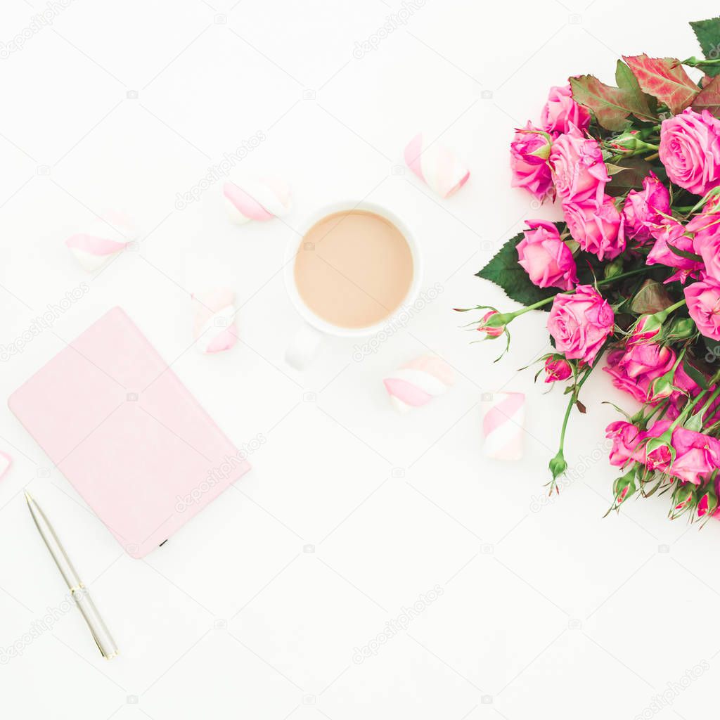 Female desk with pink roses bouquet, pink diary, coffee mug and marshmallows on white background. Flat lay. Top view