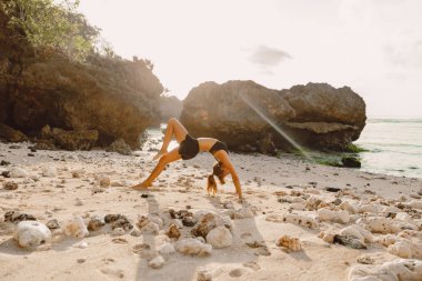 Genç kadın pratik yoga gündoğumu veya günbatımı Plajı'nda.