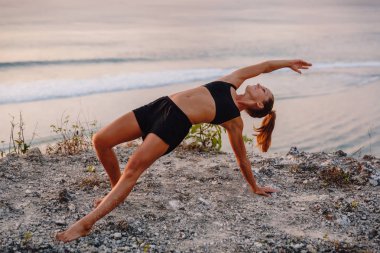 Genç kadın pratik yoga gündoğumu veya günbatımı Plajı'nda.