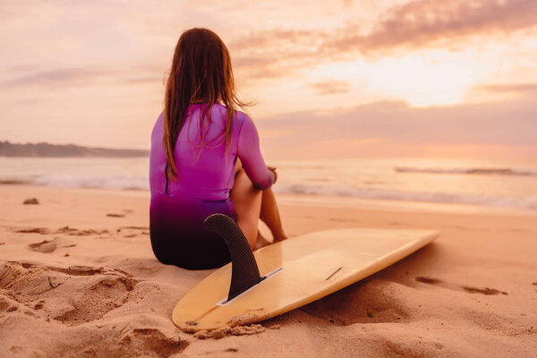 Surfer woman with surfboard on a beach at sunset or sunrise.