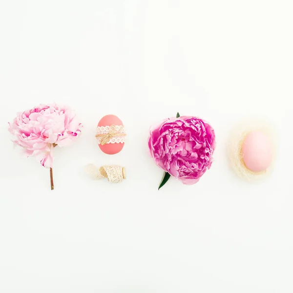 Ester festive composition with eggs, pink peonies flowers on white background. Flat lay, top view.