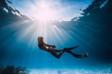 Kadın freediver yüzgeçleri ile kumlu deniz ve güneş ışınları üzerinde su altında yüzmek