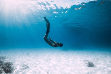 Kadın freediver yüzgeçleri ile kumlu deniz üzerinde süzülüyor. Serbest dalış mavi okyanus