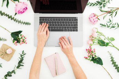 Dizüstü bilgisayarda yazarak kadın. Eller, laptop, dizüstü bilgisayar ve pembe çiçekler beyaz arka plan üzerinde ile çalışma alanı. Düz yatıyordu.