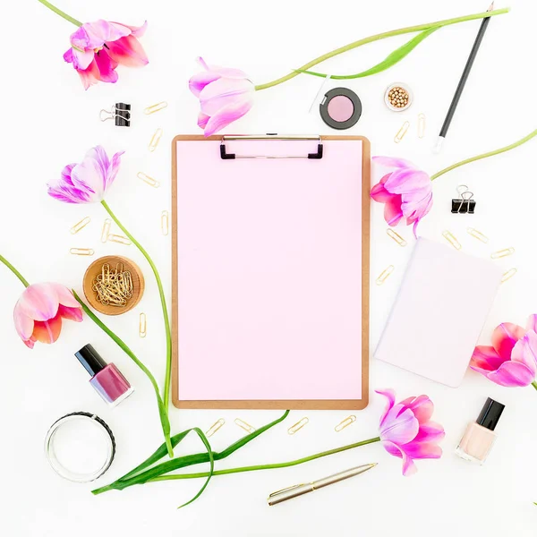 Freelance Concept with clipboard, notebook, pen, pink tulip flowers and cosmetics on white background. Flat lay, top view