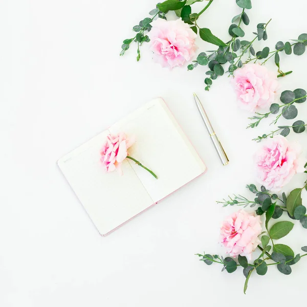 Frame of pink roses flowers and eucalyptus with diary and pen on white background. Flat lay, top view. Valentines day
