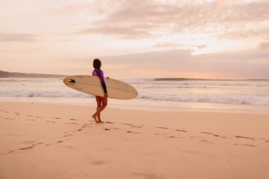 Sörfçü kız gündoğumu veya günbatımı bir plajda surfboard ile.