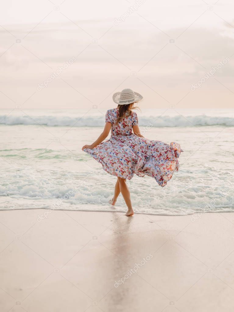 Attractive woman in summer dress on ocean beach at sunset.