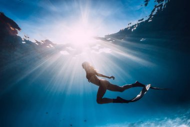 Kadın freediver yüzgeçleri ile yüzmek kumlu alt ve güneş ışınları sualtı okyanus üzerinde