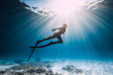 Freediver genç kadın yüzgeçleri ile kumlu alt sualtı okyanus üzerinde yüzmek