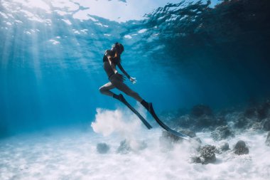 Kadın freediver yüzgeçleri ile yüzmek kumlu alt ve güneş ışınları sualtı okyanus üzerinde