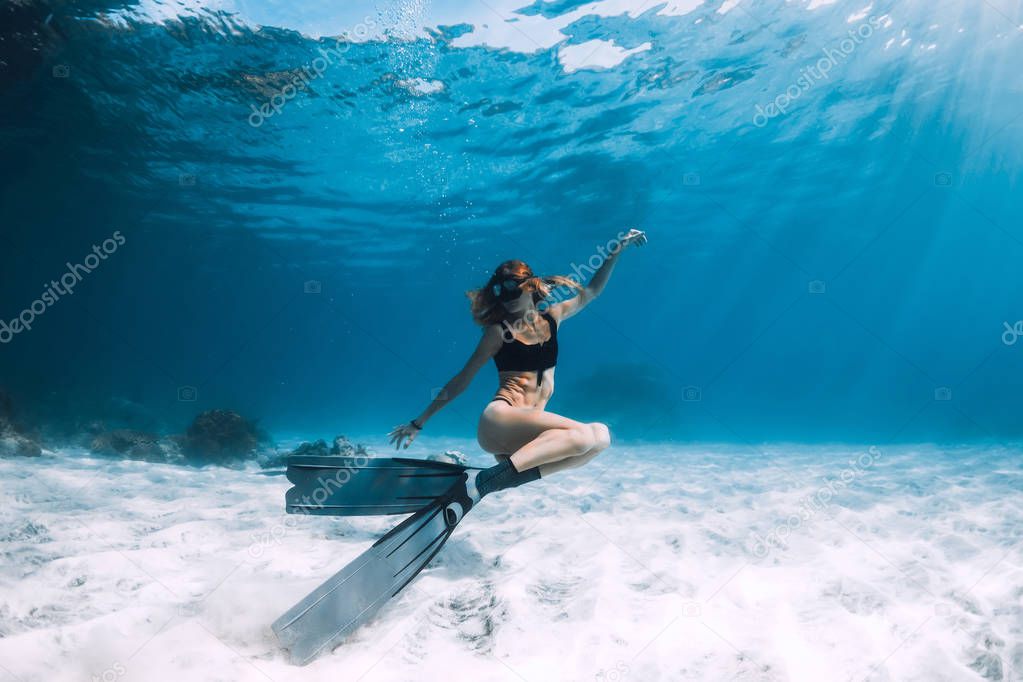Freediver young woman with fins swim over sandy bottom underwater ocean
