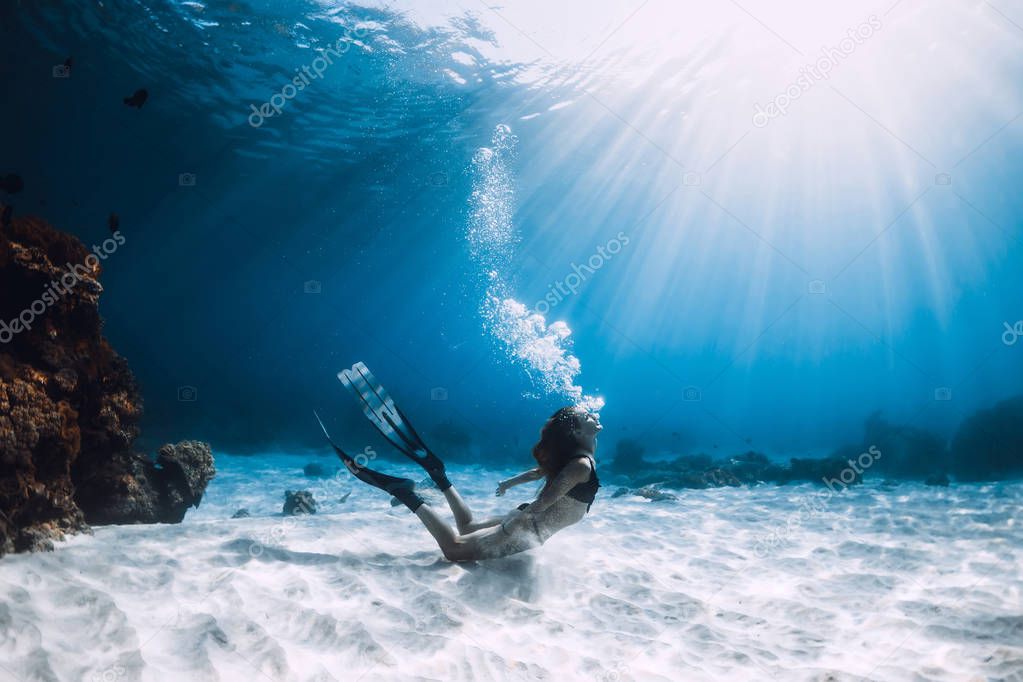 Woman freediver with fins swim over sandy bottom underwater ocean