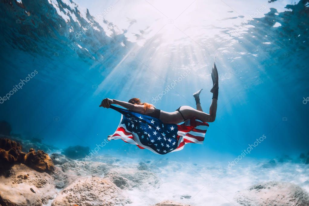Woman freediver swim over sandy sea bottom with USA flag. Independence day