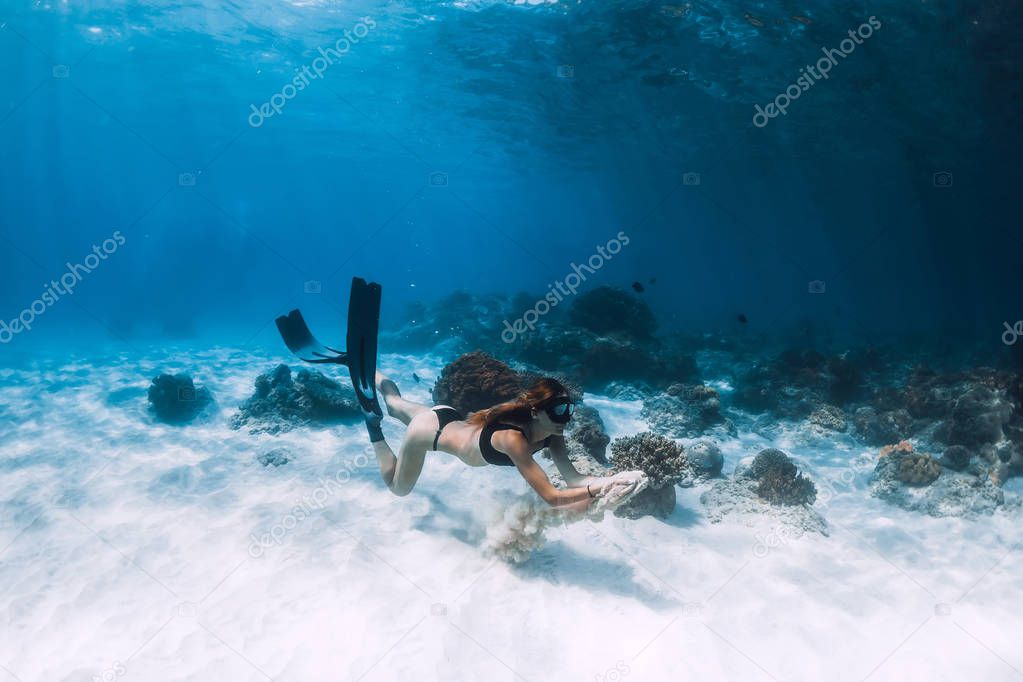 Freediver girl with fins swim over sandy bottom and sun rays underwater ocean