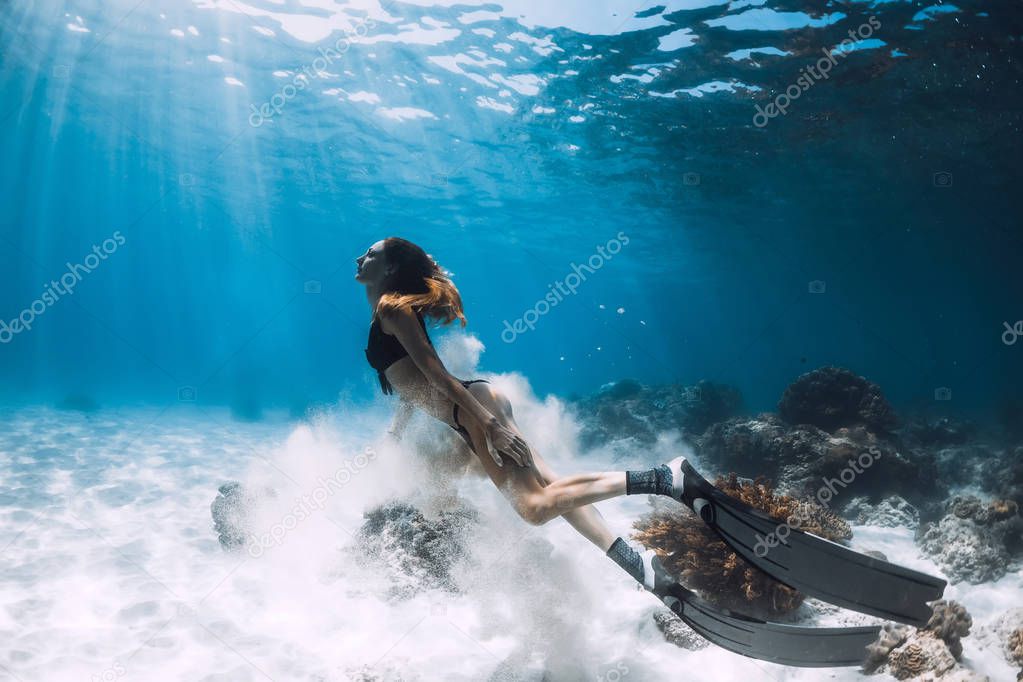 Woman freediver with fins swim over sandy bottom and sun rays underwater ocean