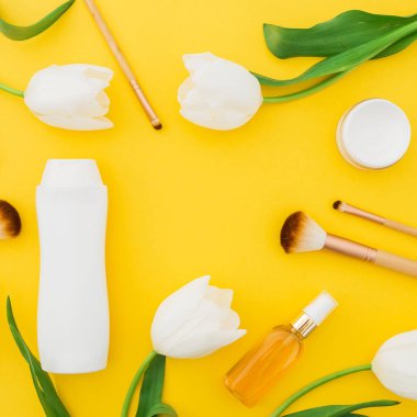 Sarı arka planda şampuan, parfüm, krem ve beyaz lale çiçekler. Düz yatıyordu, üst görünüm