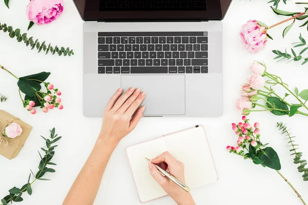 Kadın dizüstü bilgisayarda yazıyor. Kadın eller, dizüstü bilgisayar, Notebook ve beyaz pembe çiçekler ile çalışma alanı. Düz yatma.